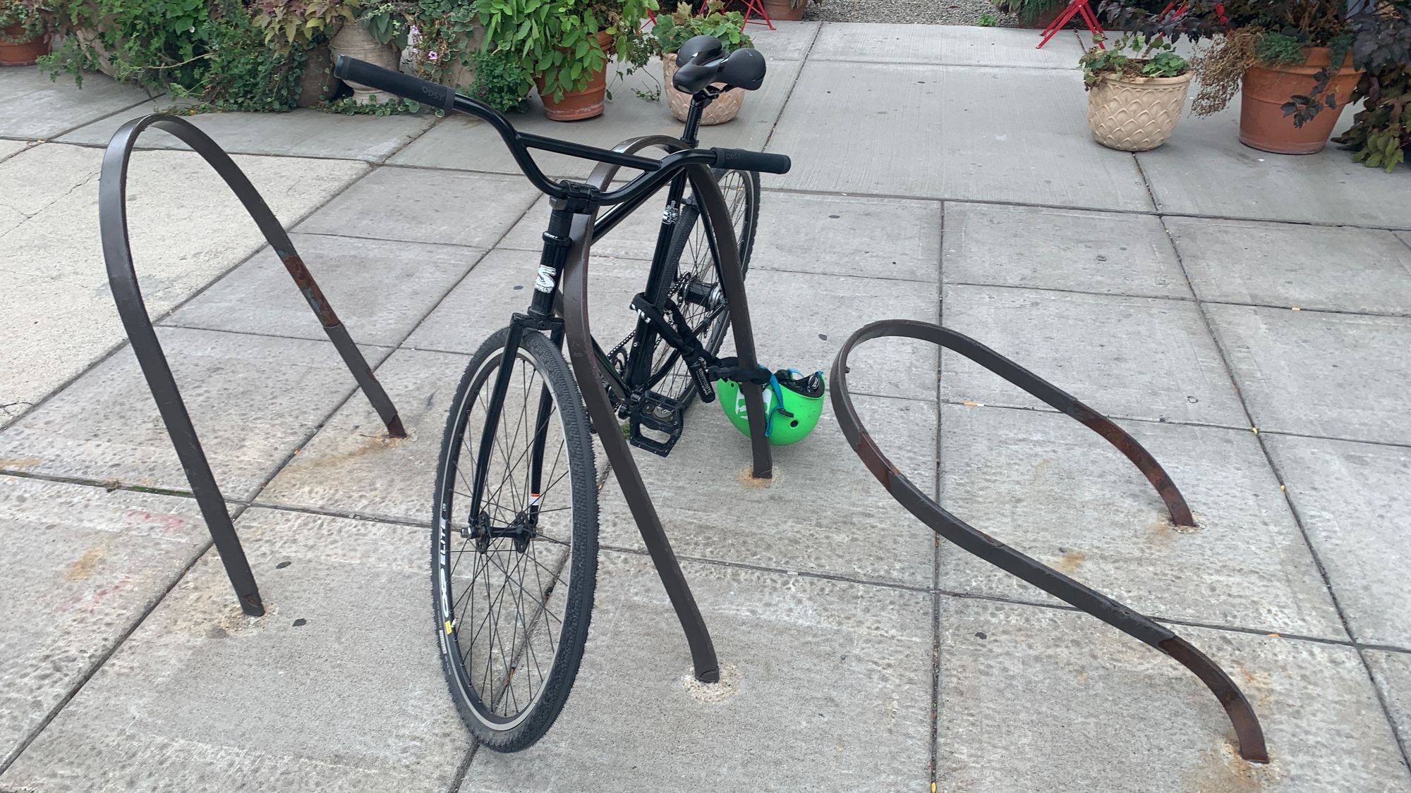 A bicycle is parked in a set of inverted u-shaped bike racks. The racks appear to have been hit by a car and are dramatically bent out of shape.
