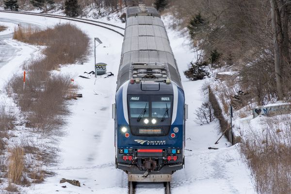 An Amtrak passenger train moves along the tracks. There is snow on the ground.
